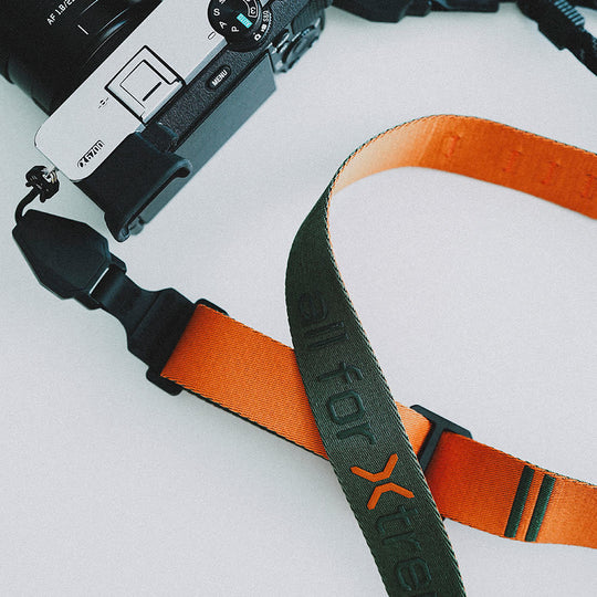 Camera with an orange and black strap on a light gray background