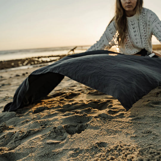 woman on sandy beach, laying out charcoal beach towel