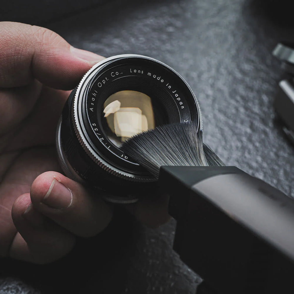 Person cleaning a camera lens with a brush