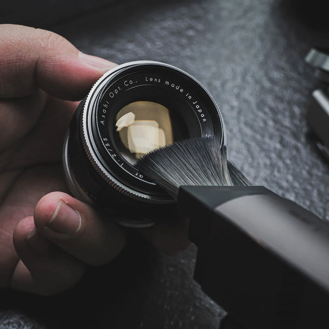 Person cleaning a camera lens with a brush