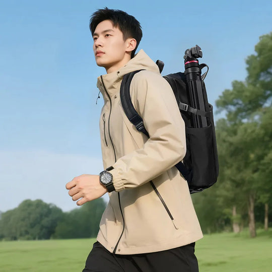 Man wearing a beige jacket and black backpack with camera equipment, standing outdoors.