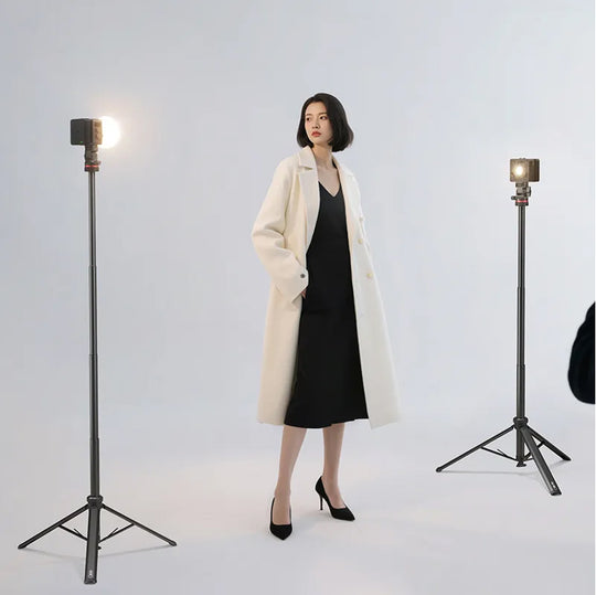 Woman in a white coat and black dress standing between two studio lights on a light gray background