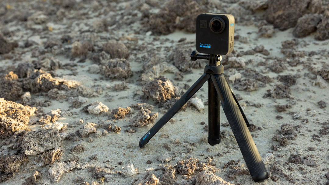 Camera on a tripod in a natural outdoor setting with rocks and sand.