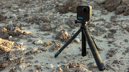 Camera on a tripod in a natural outdoor setting with rocks and sand.