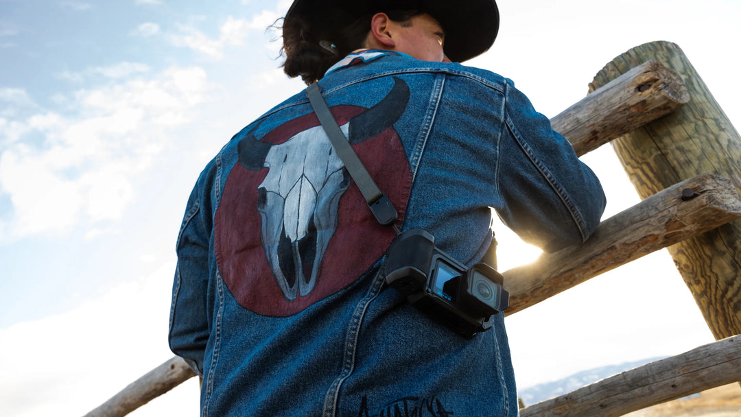 Person wearing a blue denim jacket with a horse skull design, standing near a wooden fence.