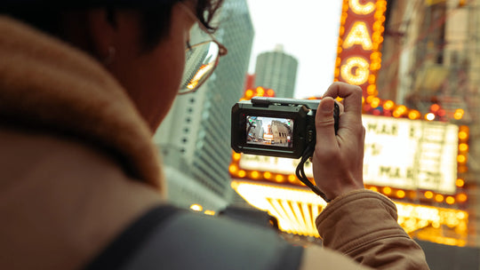 Person taking a photo with a camera in front of a cityscape with neon signs