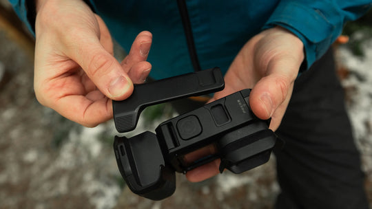 Person holding a black camera grip with a blurred natural background