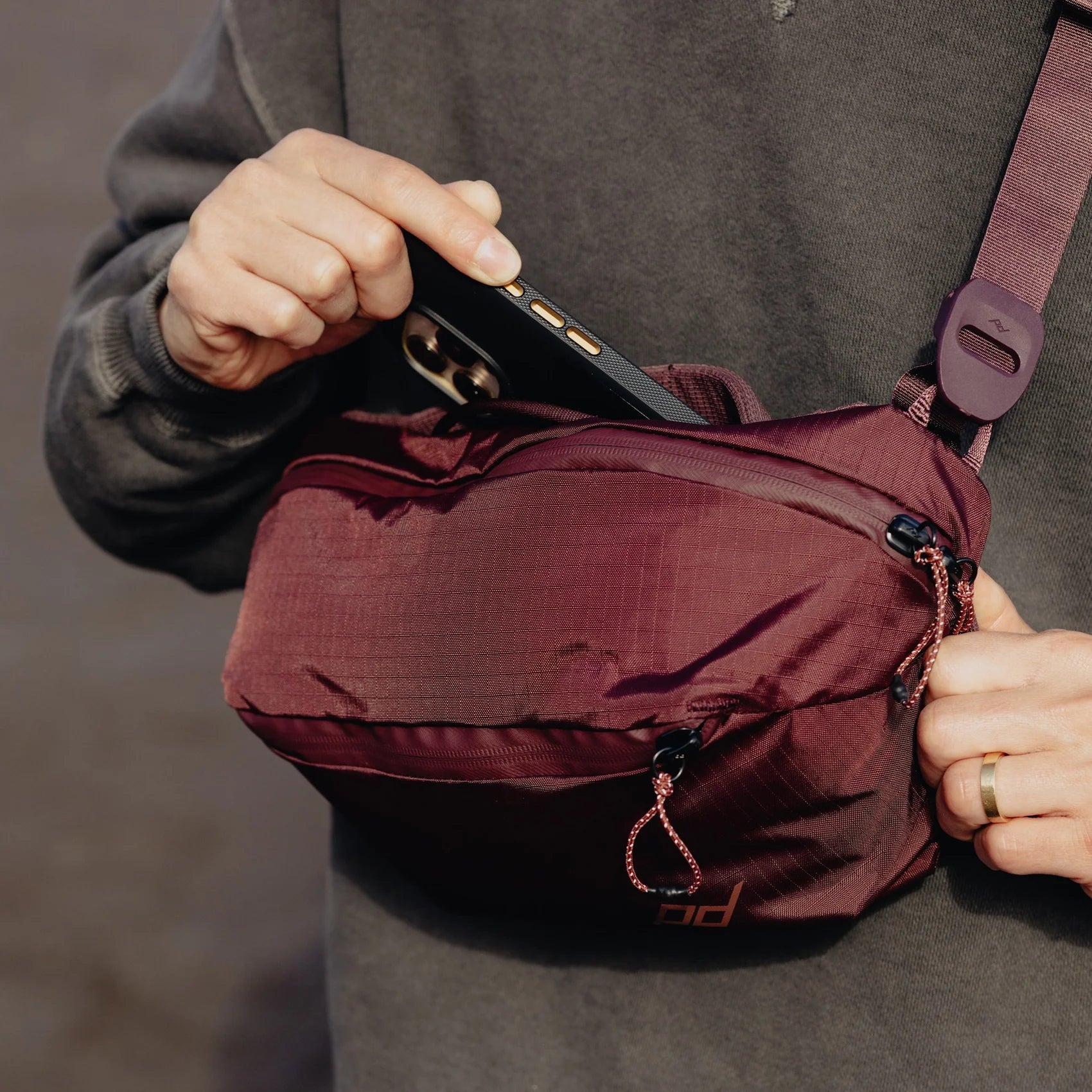 Person holding a phone over a maroon waist bag against a dark background