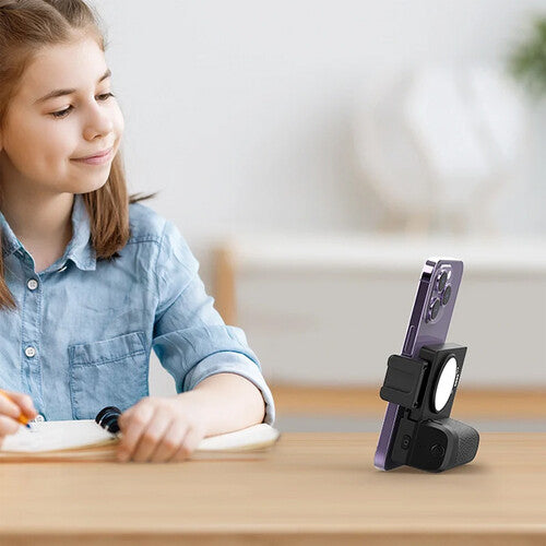 Young girl using a smartphone with a stand on a table, possibly for educational purposes.