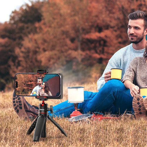 Man sitting outdoors with a smartphone on a tripod, showing a video call with a woman.