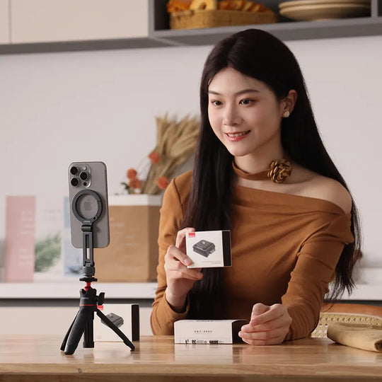 Woman holding a product box with a smartphone on a tripod in a kitchen setting