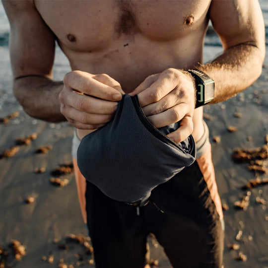 Man on a beach wearing a black glove and watch, with a blurred background.