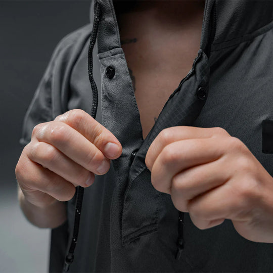 Person wearing a NanoDry Packable Towel Poncho with hands adjusting the zipper against a dark background
