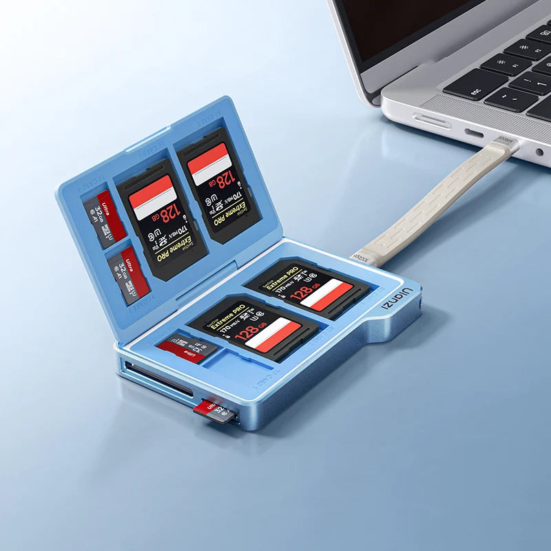 A light blue USB card reader and writer holding multiple SD cards, shown open on a light blue surface with part of a laptop visible in the upper right.