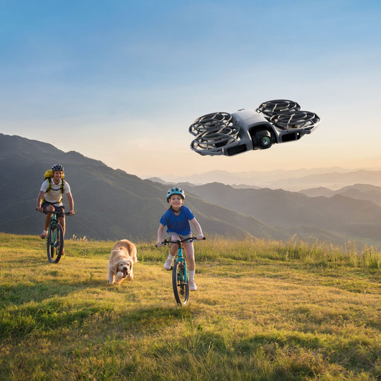 Two children on bicycles with a dog, a drone flying above them in a mountainous landscape.