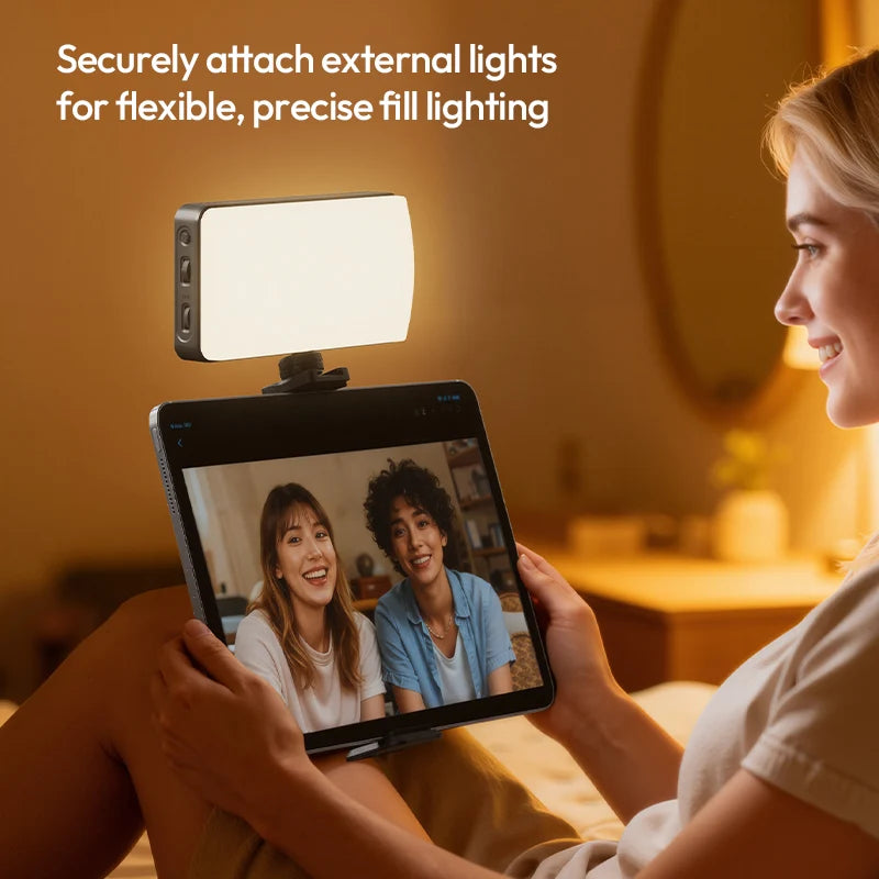 Person using a tablet with a light attached for video call, in a warm indoor setting.