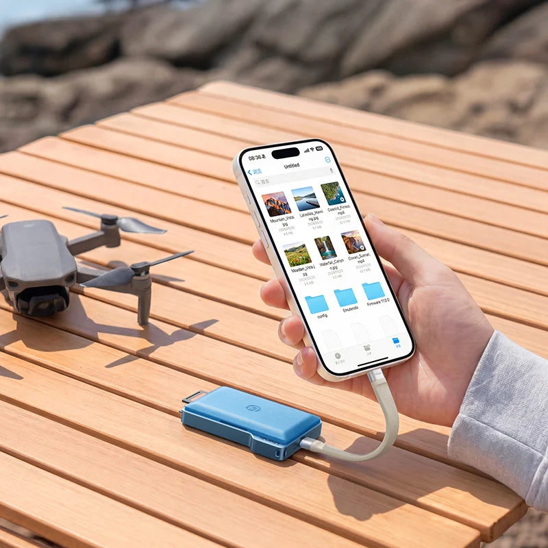 Person using a smartphone with a blue USB device on a wooden surface, with a drone in the background.