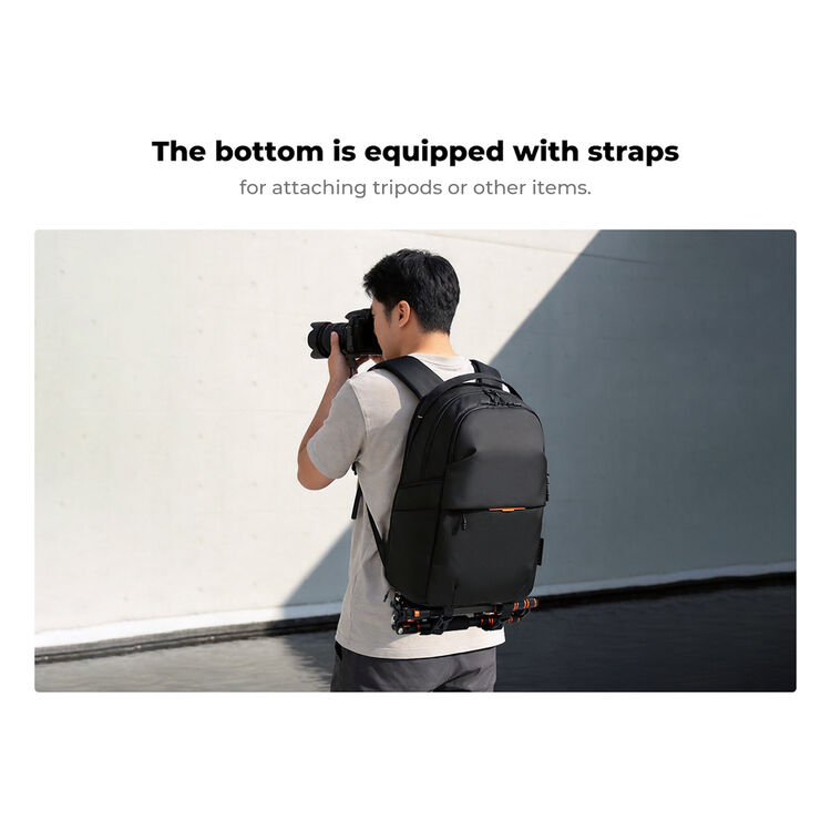 A man wearing a black backpack with attached camera straps, holding a camera against a light gray wall. Text above reads, &