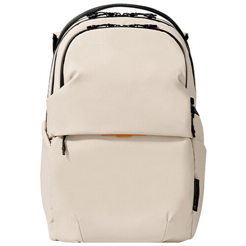 A minimalist beige backpack with black zippers and trim, shown against a plain white background.