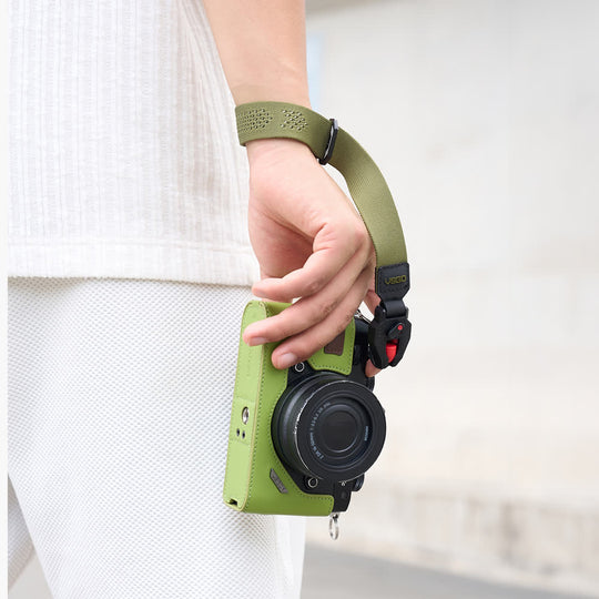 Green camera case with VSGO Black Snipe CASUAL Lightweight Camera Wrist Strap held by a person against a white background