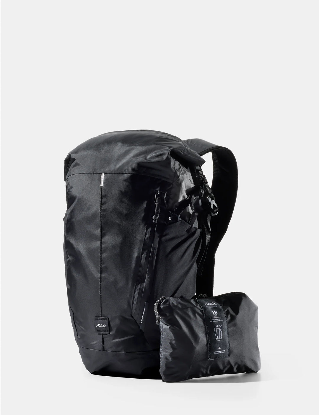 A black waterproof backpack shown with its matching black rolled storage pouch in front, photographed on a clean light gray studio background.
