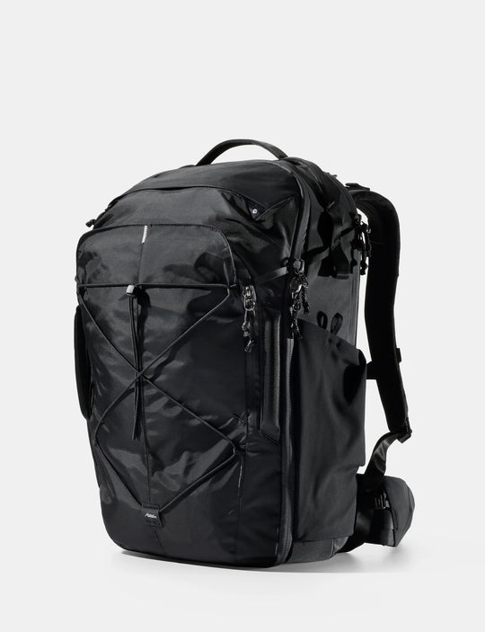 A black technical backpack with multiple zippered compartments, compression straps, and padded shoulder straps, shown from a three-quarter angle on a light gray background.