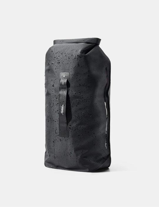 A black waterproof dry bag with a roll-top closure, covered in water droplets, featuring a vertical black strap with a white logo on the front, set against a light gray background.