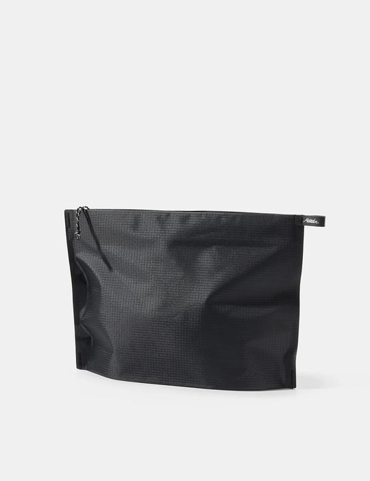 A black textured zippered pouch with a small black brand tab on the right side, photographed on a clean light gray background.