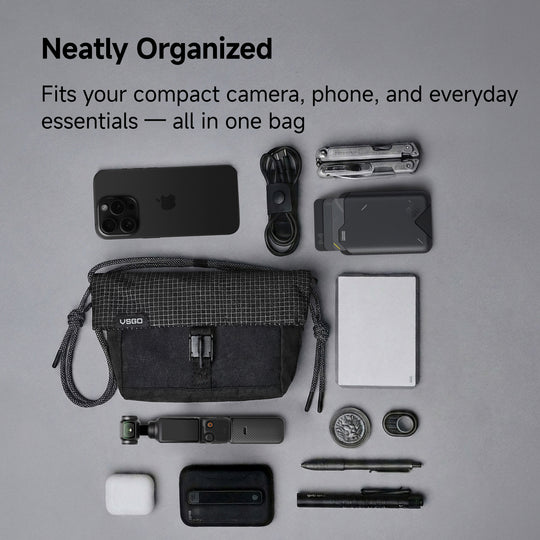 Black bag with various items including a phone, camera, and accessories on a gray background