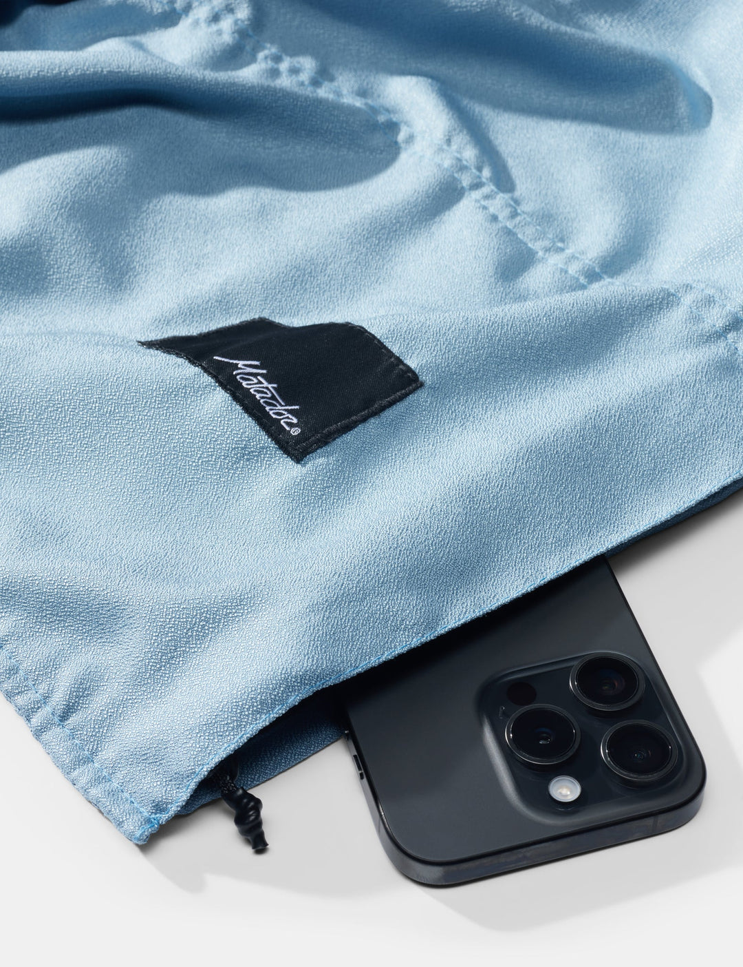 Blue towel with a matador brand logo and a smartphone underneath on a white background