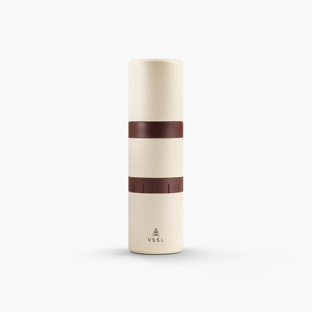 A minimalist cylindrical travel tumbler in cream with two dark brown bands, featuring the VSSL logo near the bottom, set against a clean white background.