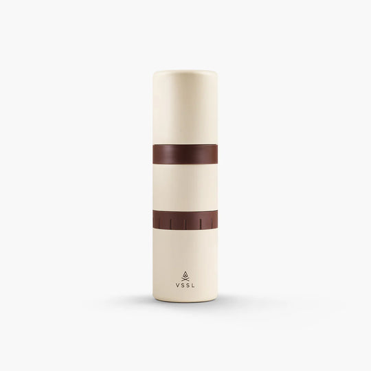 A minimalist cylindrical travel tumbler in cream with two dark brown bands, featuring the VSSL logo near the bottom, set against a clean white background.