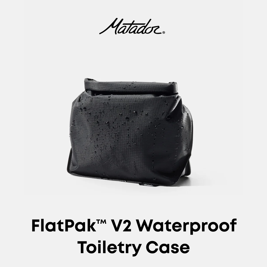Matador FlatPak V2 Waterproof Toiletry Case in black textured material, shown with water droplets on its surface against a light gray background with product text.