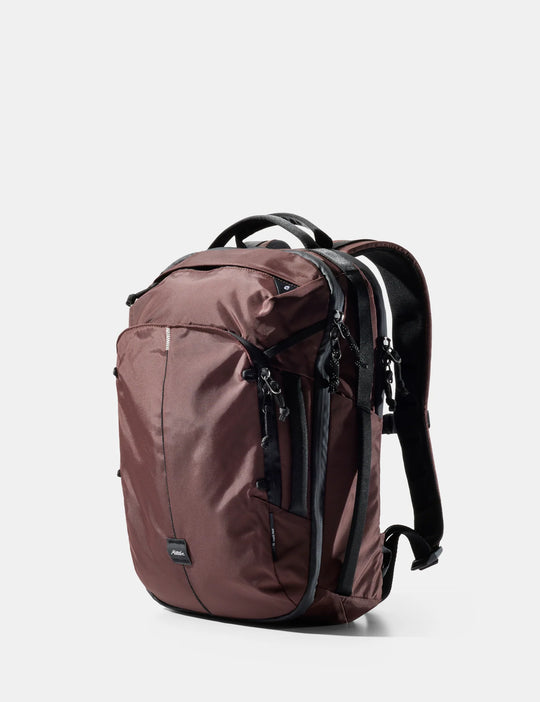 A dark brown nylon backpack with black zippers, handles, and shoulder straps, shown from a three-quarters angle on a light gray background.