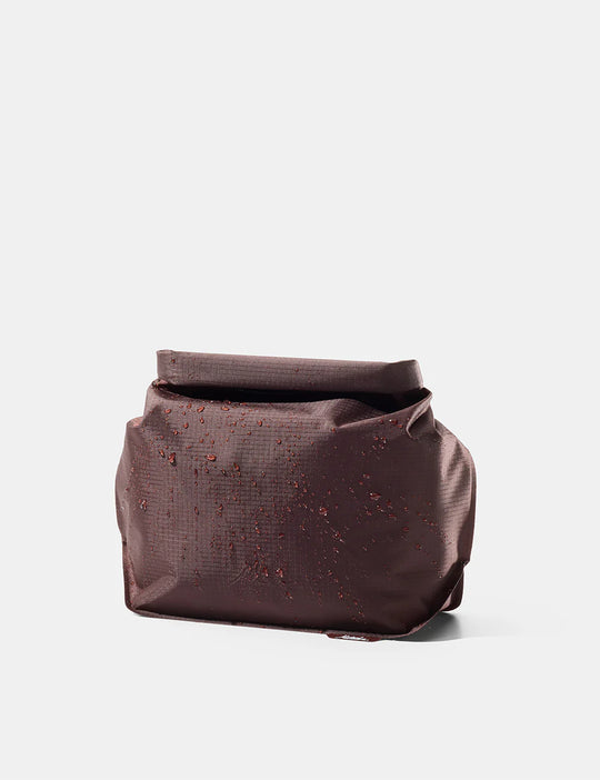 A dark brown textured cosmetic pouch with a rolled top flap, shown on a clean light gray background.