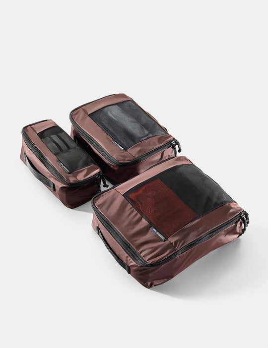 Set of three brown travel packing cubes on a light gray background