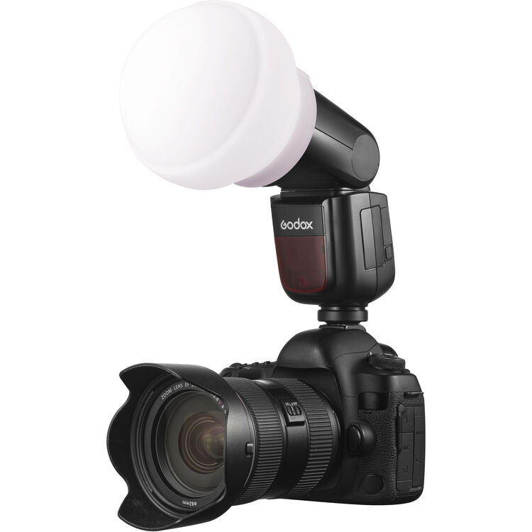 A black Godox camera flash with a white diffuser attached to a DSLR camera with a lens, shown against a plain white background.