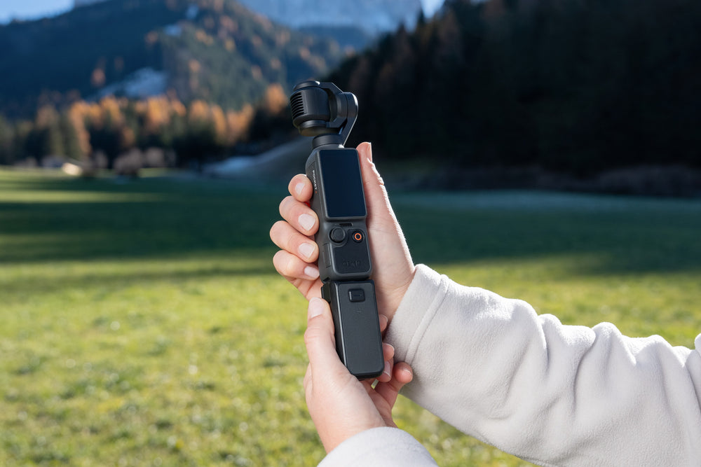 Hand holding a dji osmo pocket 4 with a scenic background of mountains and trees.