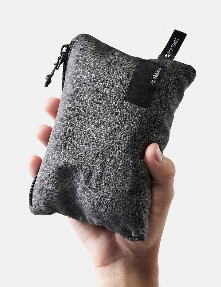 Gray zippered pouch held in a hand with a visible brand label on a light gray background
