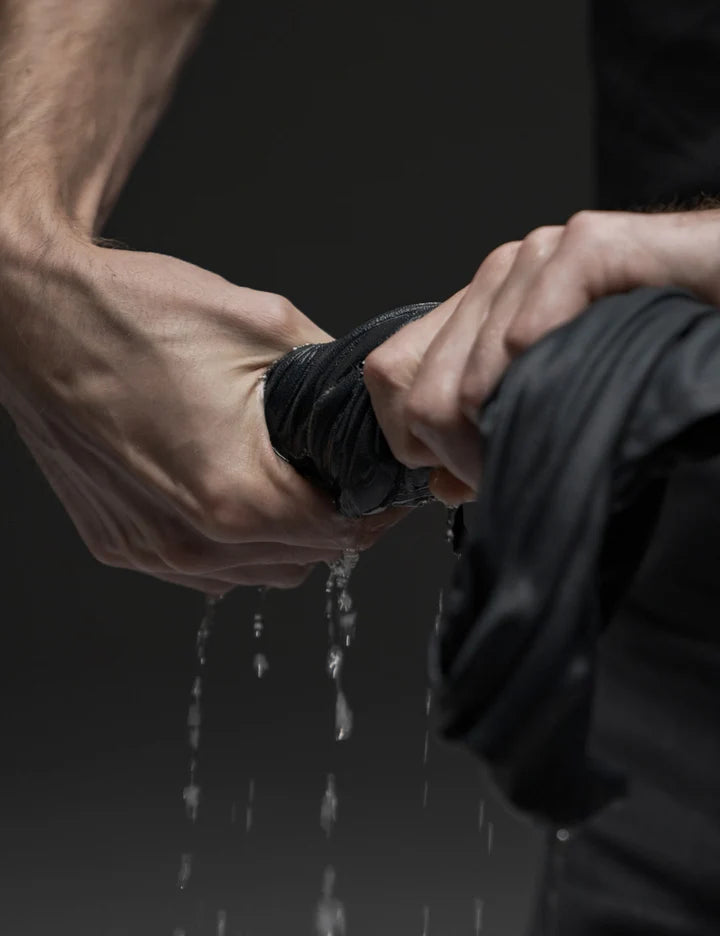 Two hands holding a black rubber band over water with a dark background