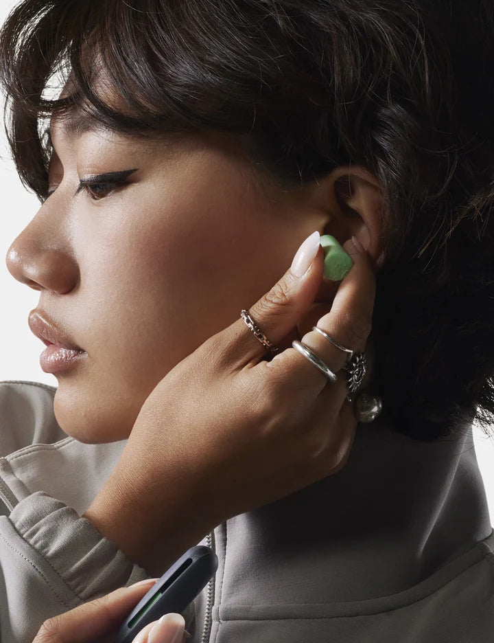 Woman wearing a green earring with a neutral background