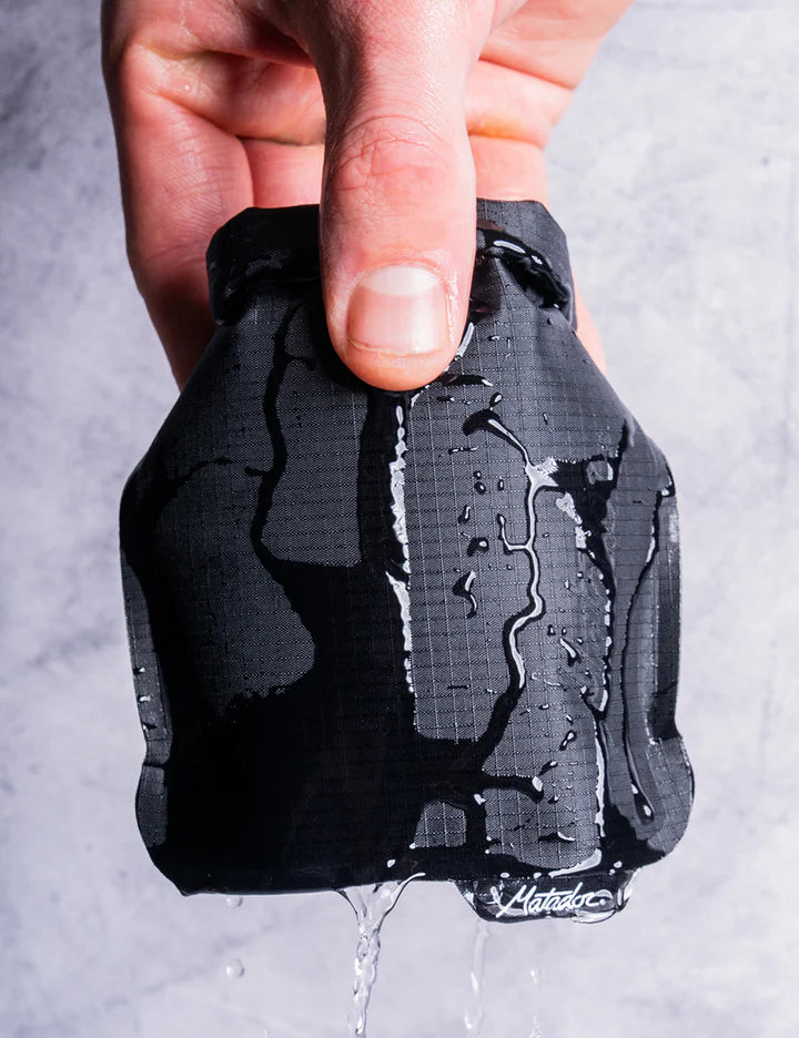 Hand holding a black glove with water dripping off it against a gray background