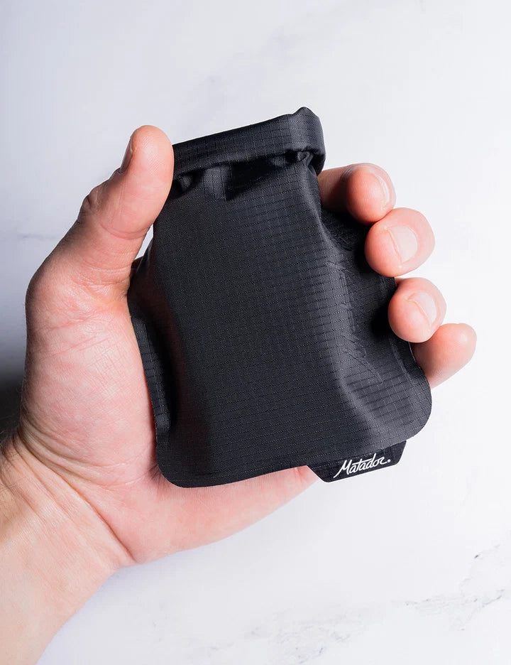 Hand holding a black textured pouch with 'Harkila' branding on a light gray background