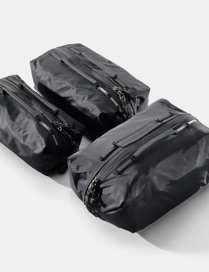 Three black waterproof dry bags of different sizes arranged diagonally on a light gray background.