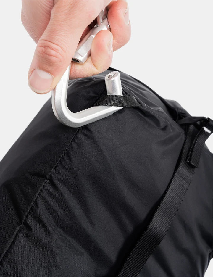 A close-up of a hand attaching a silver carabiner to a black bag with a black strap and loop.