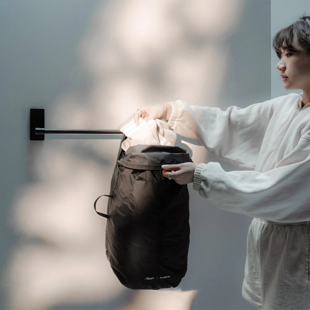 Person in a white robe interacting with a black Packable Laundry Bag against a neutral background