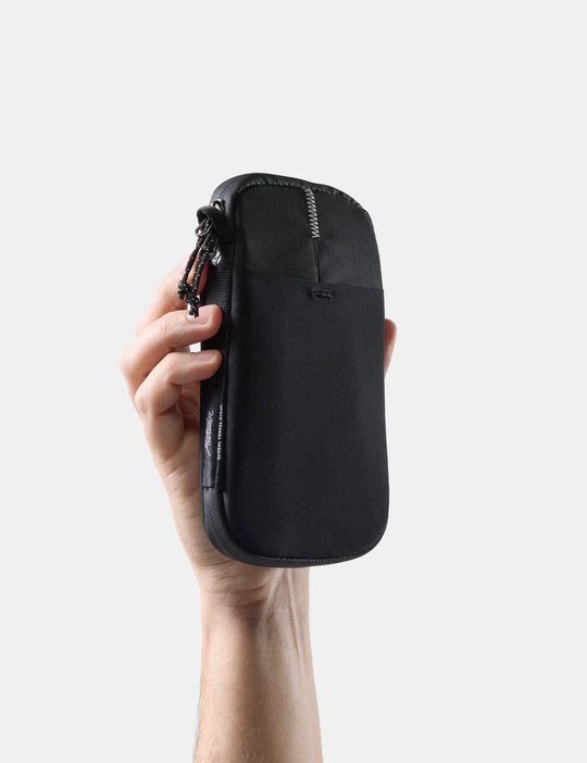 Hand holding a black Global Travel Stash against a light gray background