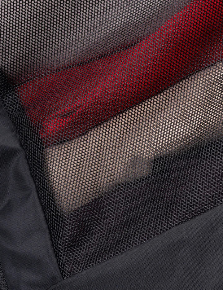 Close-up of a black mesh pocket containing folded garments, including a prominent red item and a beige item, with a black fabric border visible around the edge.