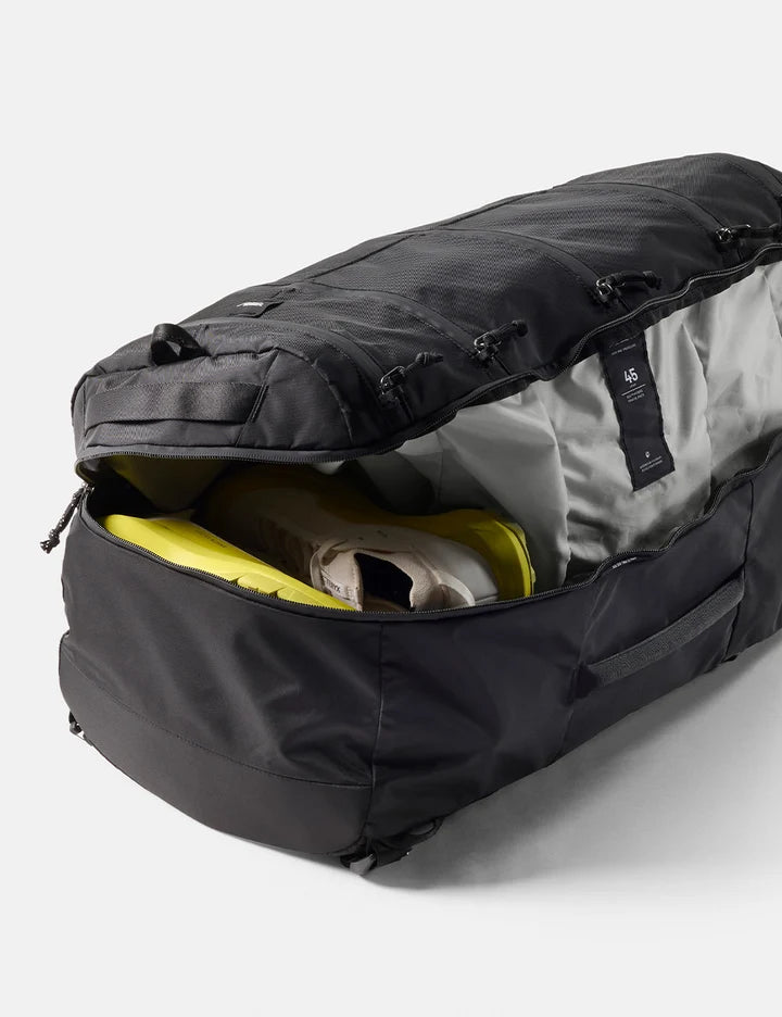 A black duffel bag shown open, revealing a light gray interior lining and a bright yellow travel item inside, photographed on a clean light gray studio background.