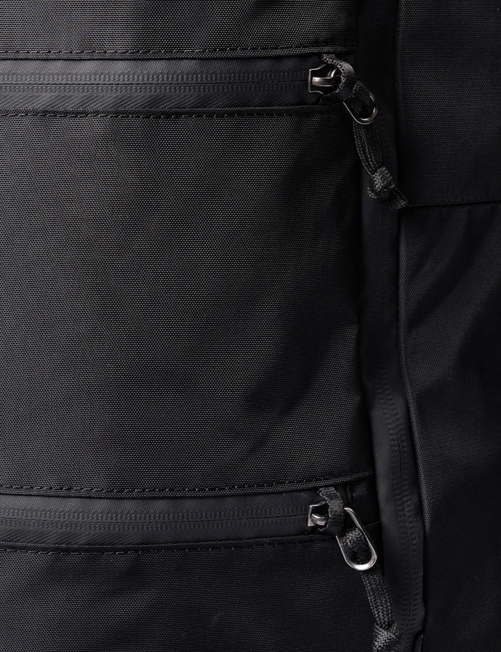 Close-up of a black fabric backpack or bag showing two horizontal zippered pockets with silver metal zipper pulls and black webbed zipper cords.